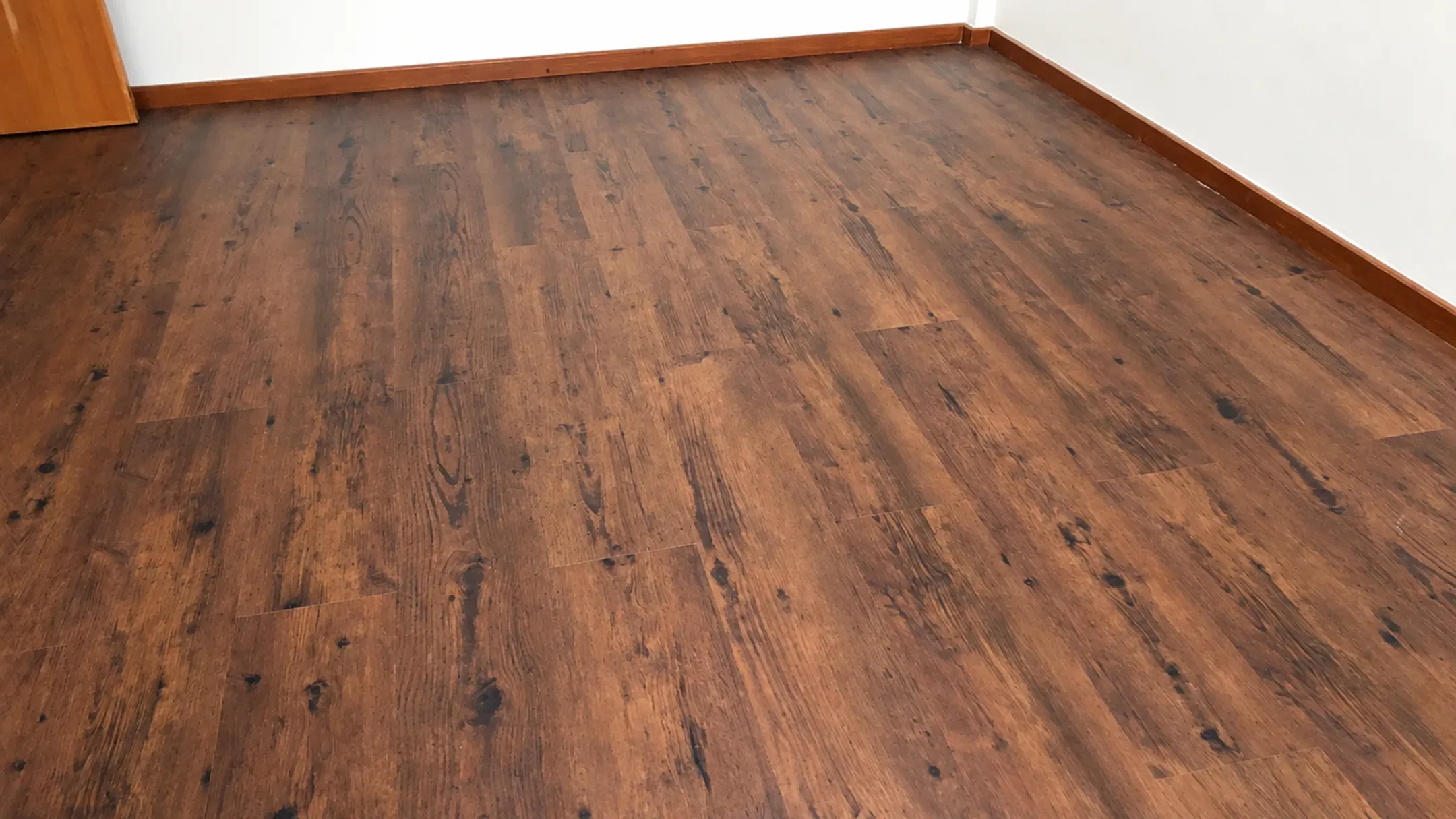 Foto pemasangan lantai vinyl motif kayu rustic cokelat tua di ruangan kosong