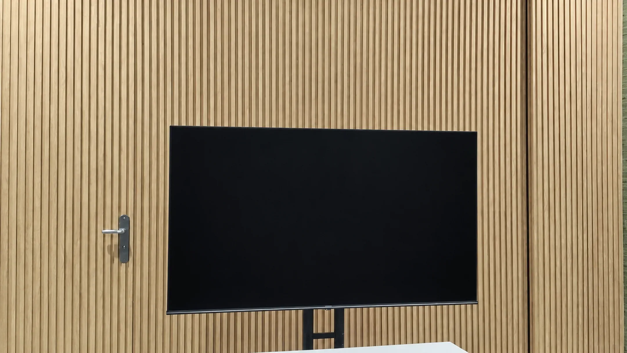 Foto pemasangan panel dinding motif kayu oak terang yang menutup dinding ruangan dengan layar TV di tengahnya